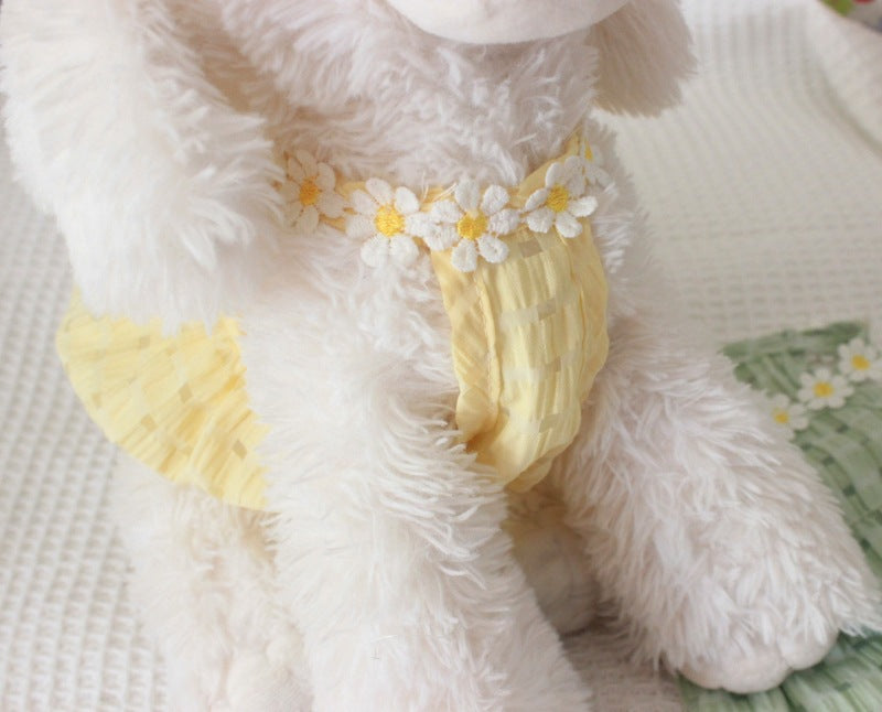 Close-up of a fluffy white lamb toy with yellow legs and floral decorations on a soft surface.