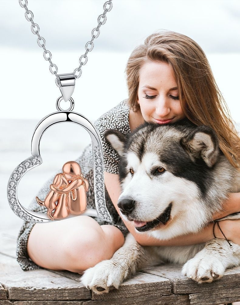 Woman holding a dog with a heart-shaped necklace featuring a small dog figure.