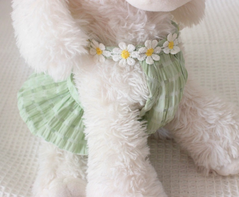 Fluffy white teddy bear wearing a green dress with flower decorations on a soft surface.