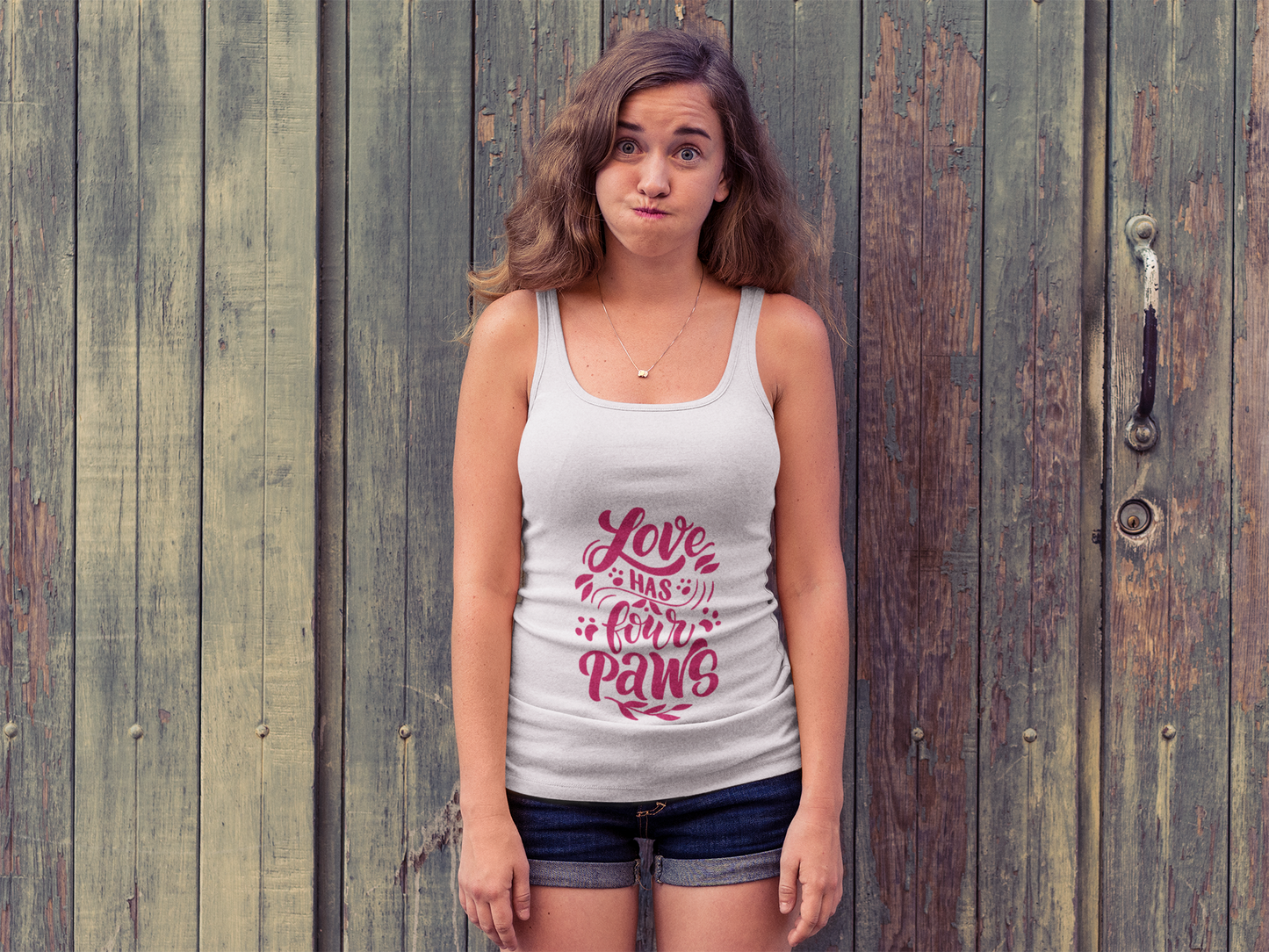 Printify white tank top with Love Has Four Paws graphic worn by woman standing in front of wooden doors