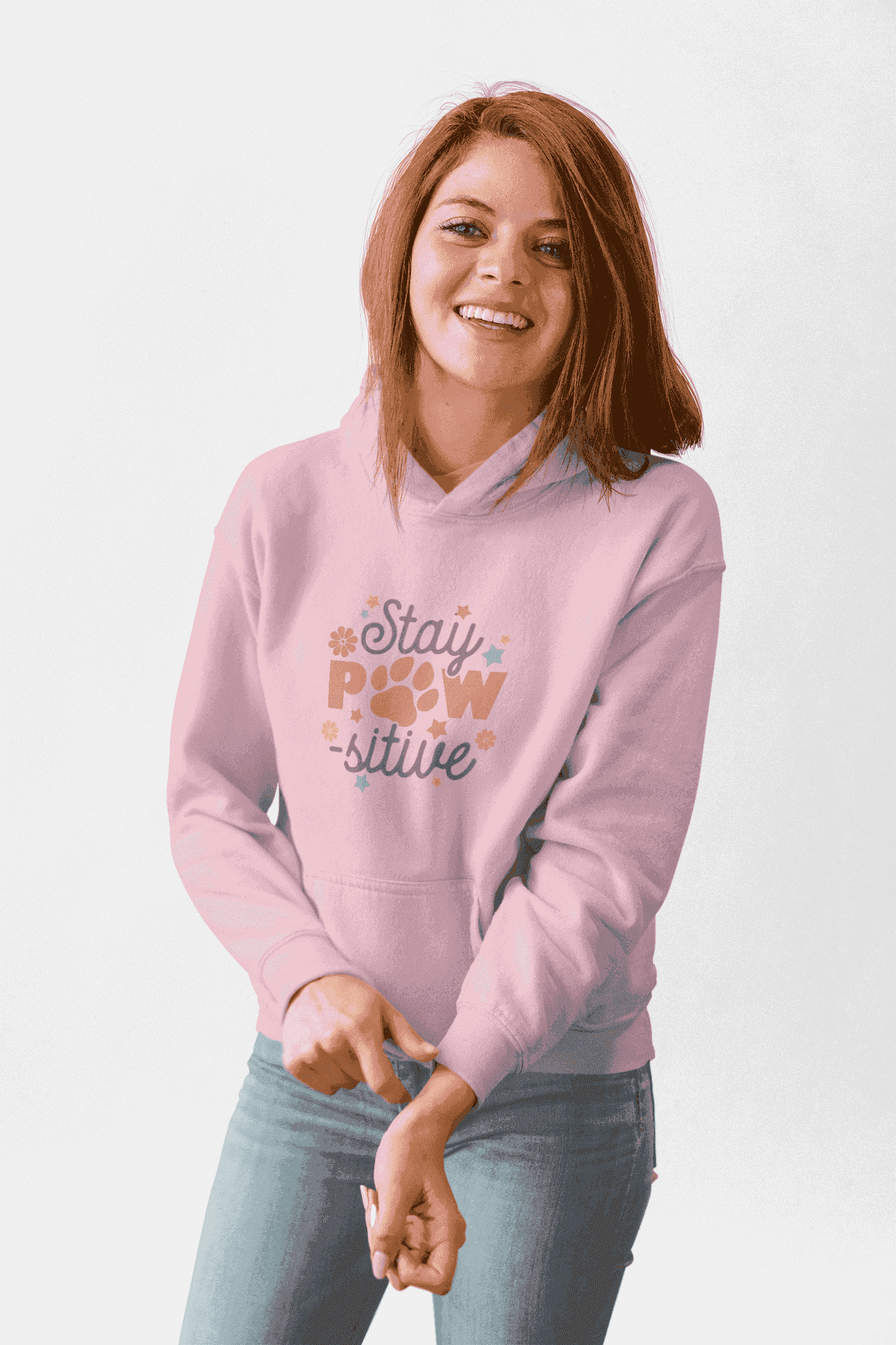 Smiling woman wearing light pink Stay Pawsitive Unisex Hoodie with paw print graphic and kangaroo pocket