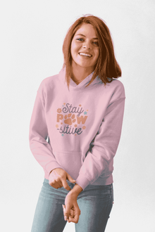 Smiling woman wearing light pink Stay Pawsitive Unisex Hoodie with paw print graphic and kangaroo pocket