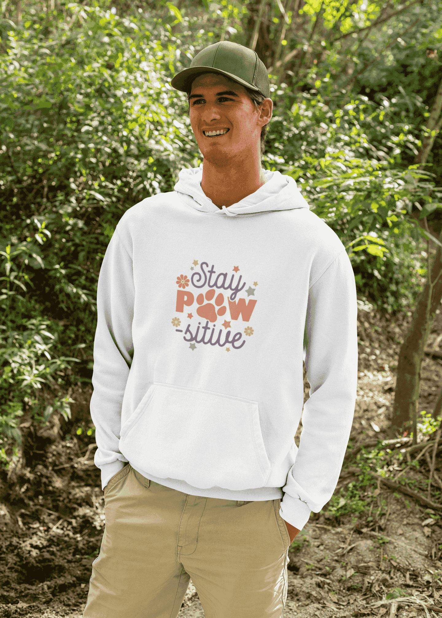 Smiling man outdoors wearing a white Stay Pawsitive Unisex Hoodie with paw graphic on chest and kangaroo pocket