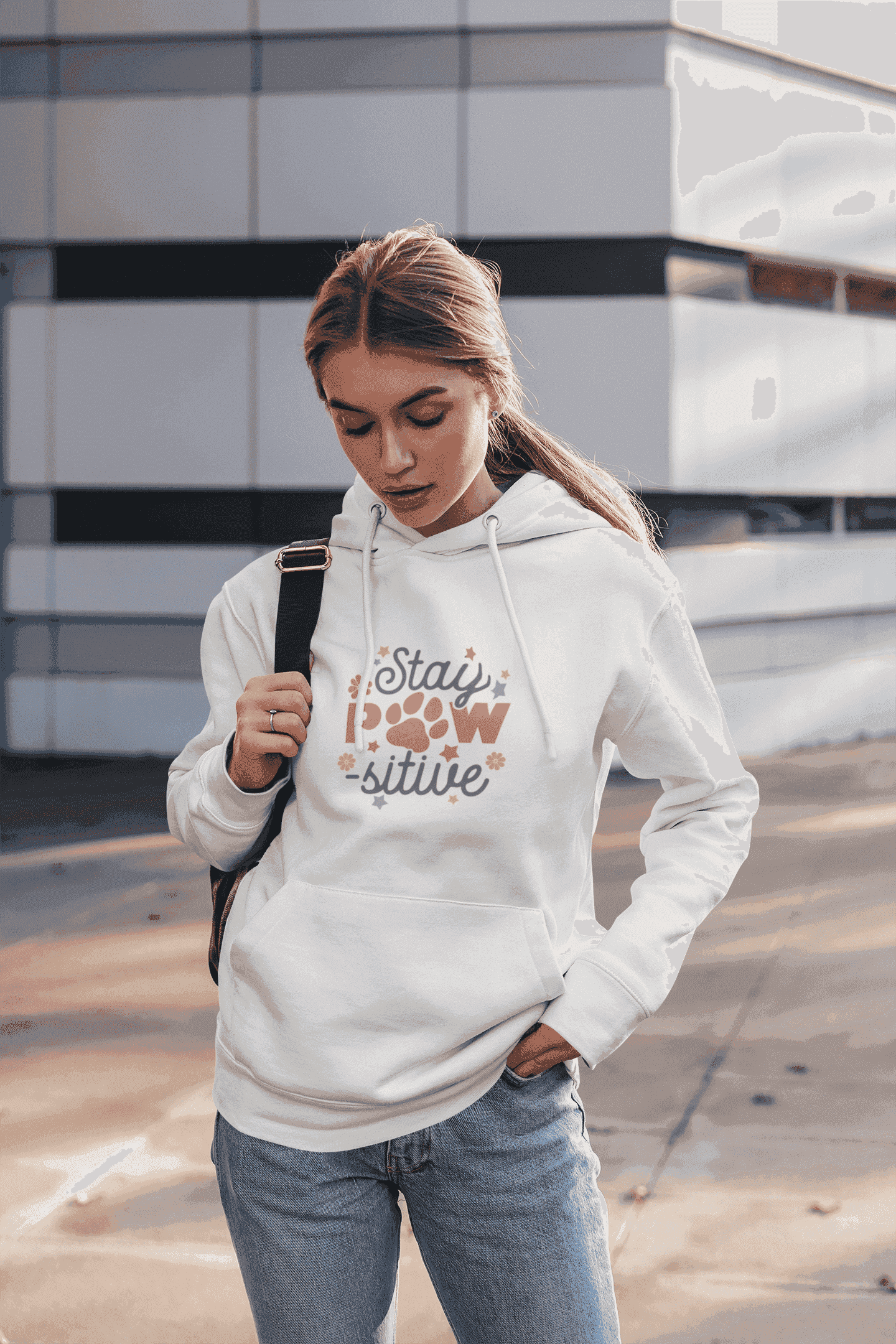 Young woman wearing Printify white Stay Pawsitive Unisex Hoodie with paw print design and kangaroo pocket