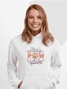 Smiling woman wearing white Stay Pawsitive Unisex Hoodie with paw print design and kangaroo pocket