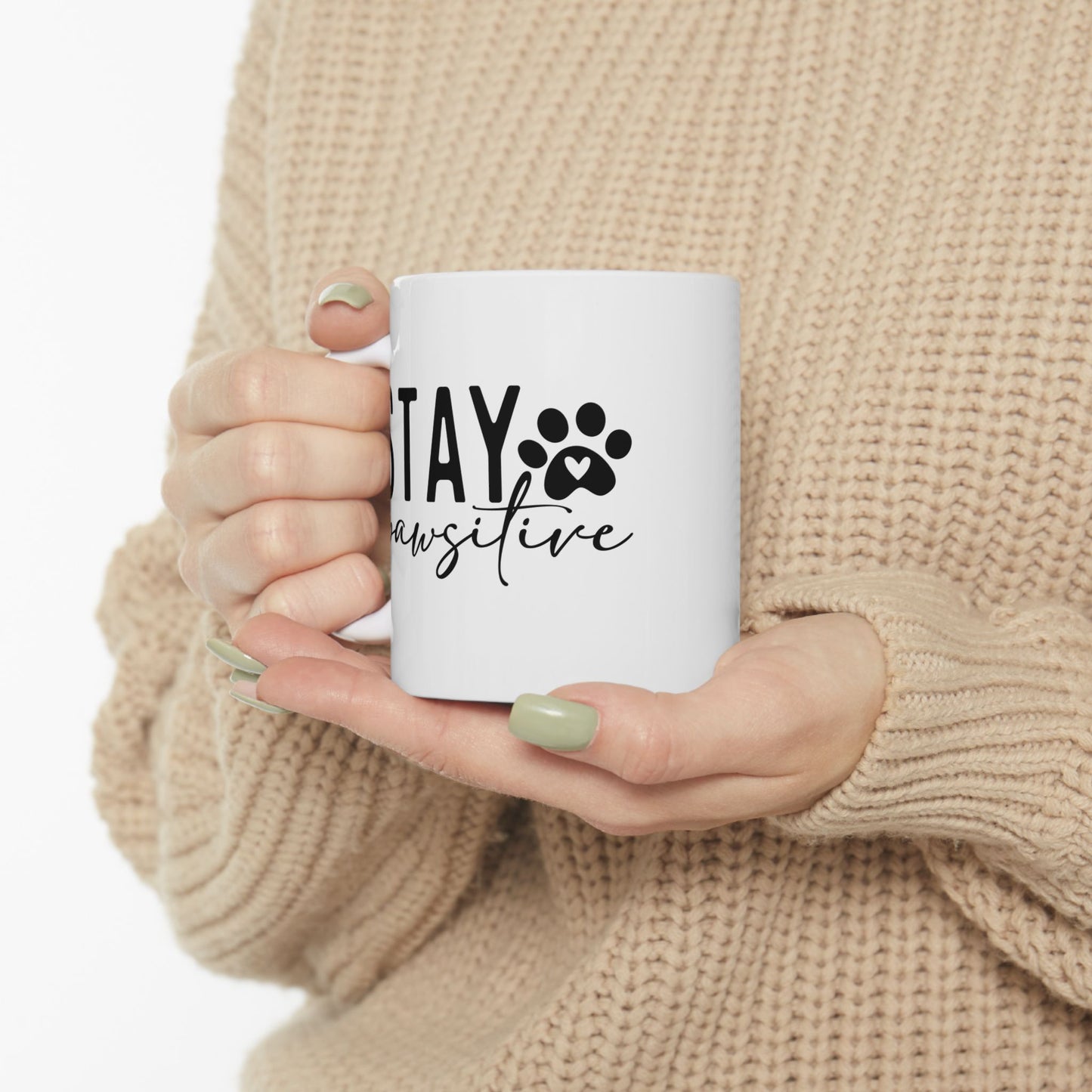 White ceramic Stay Pawsitive Mug held by person wearing beige sweater with green nails