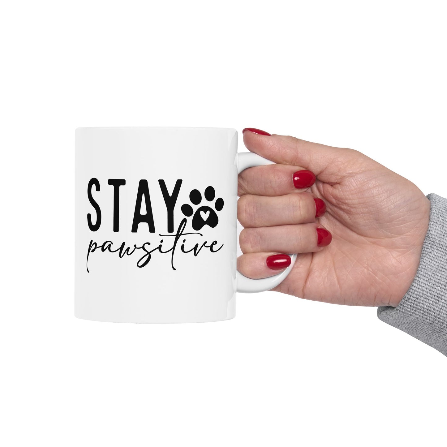 White Stay Pawsitive Mug with black text and paw print design held by hand with red nails