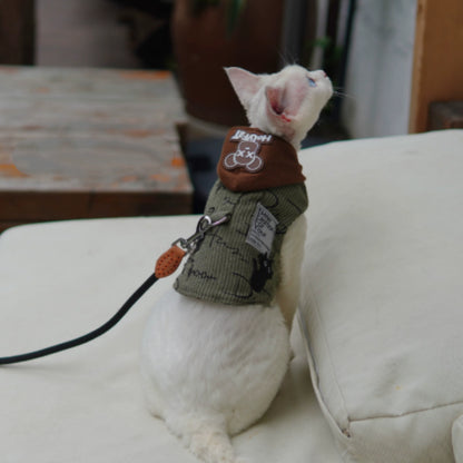 White cat wearing a brown and green outfit on a white surface