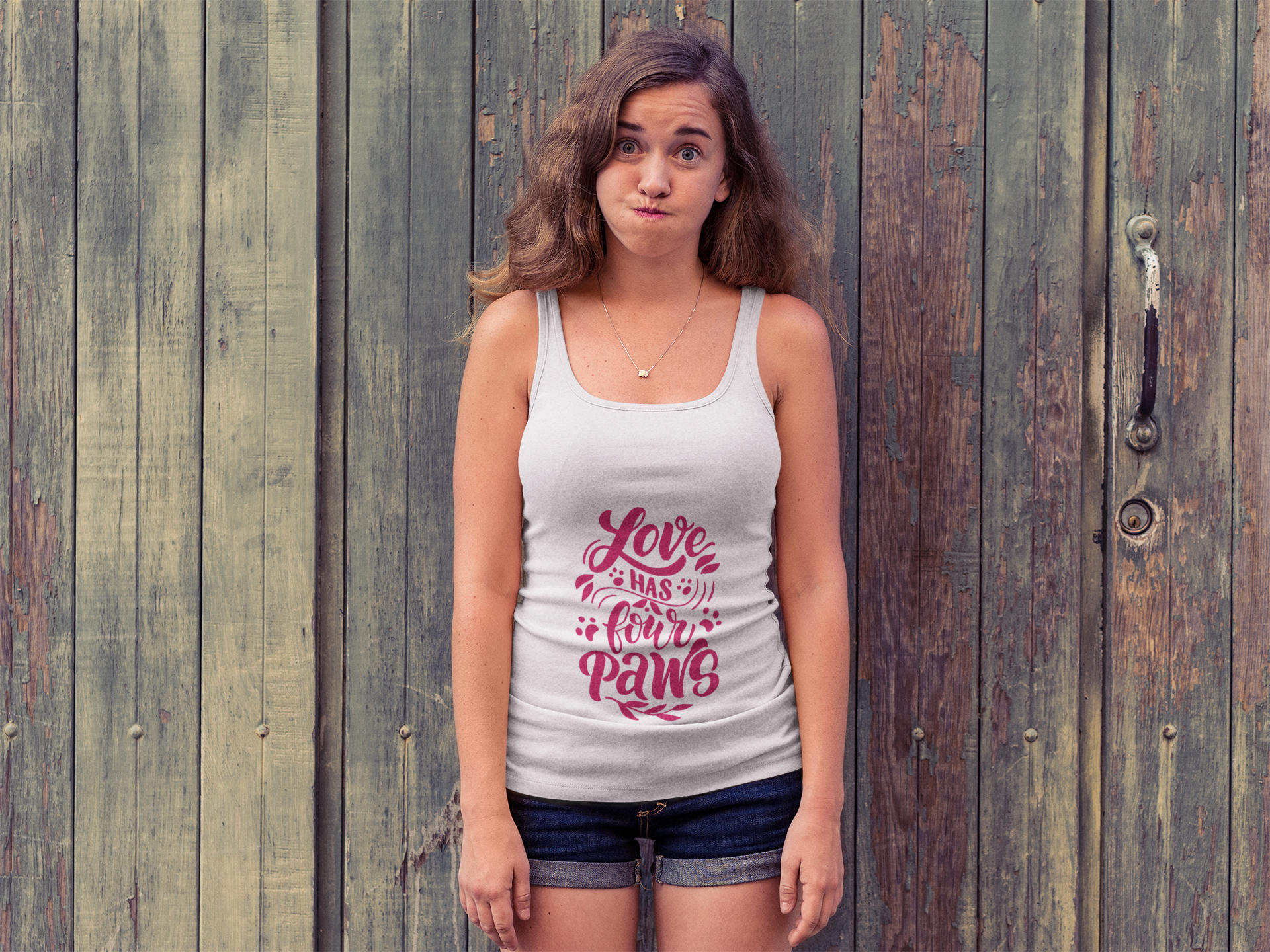 Printify white tank top with Love Has Four Paws graphic worn by woman standing in front of wooden doors