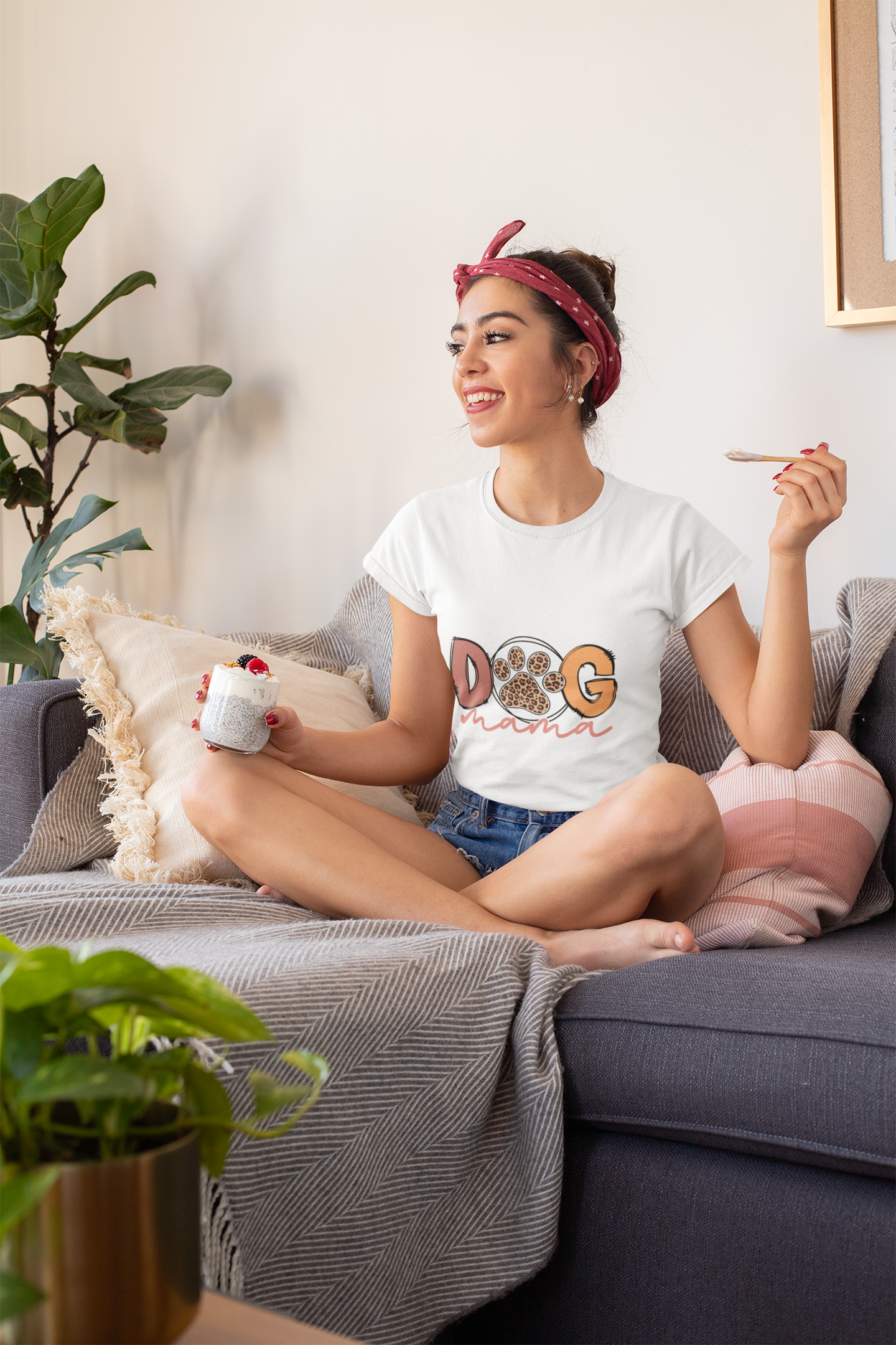 Woman relaxing on sofa wearing a white Dog Mama Tee with paw print design holding yogurt and spoon