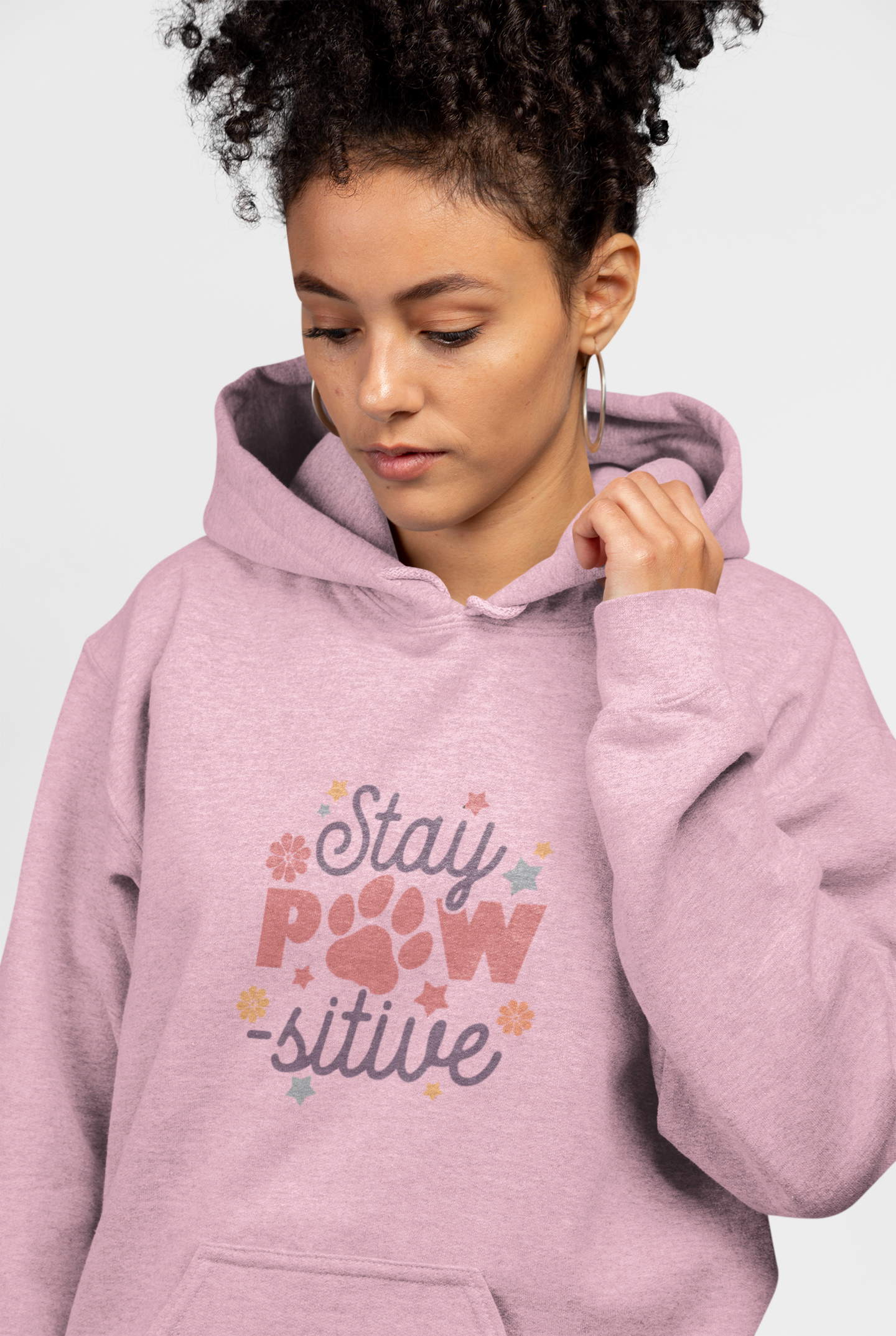 Stay Pawsitive Unisex Hoodie worn by woman model in pink with paw print graphic and kangaroo pocket