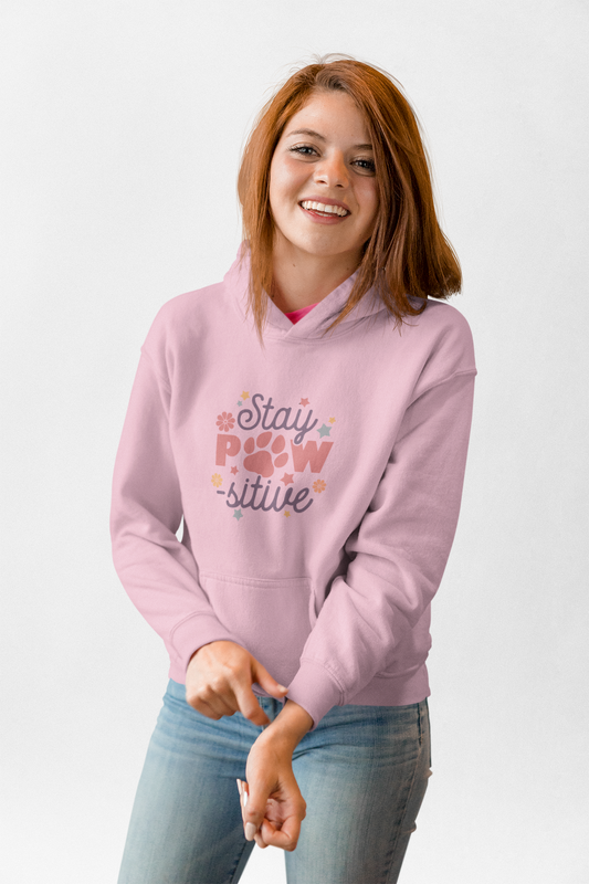 Smiling woman wearing light pink Stay Pawsitive Unisex Hoodie with paw print graphic and kangaroo pocket
