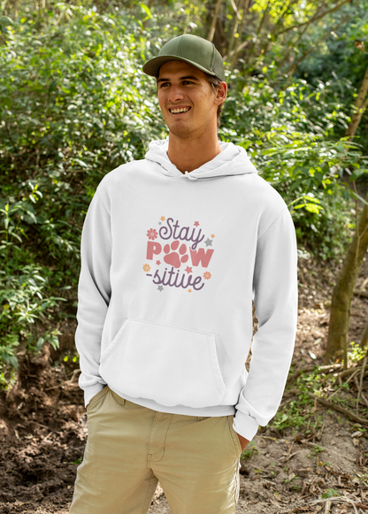 Smiling man outdoors wearing a white Stay Pawsitive Unisex Hoodie with paw graphic on chest and kangaroo pocket