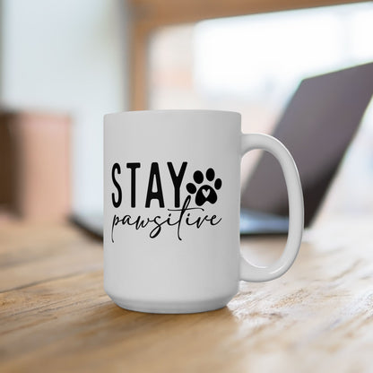 White ceramic Stay Pawsitive Mug with black paw print and heart design on wooden table